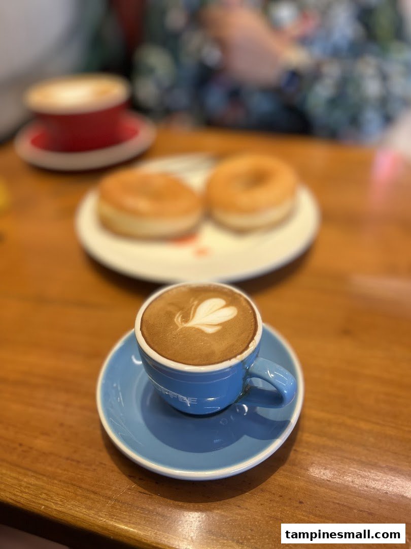 A latte with heart-shaped latte art and two donuts on a wooden table.