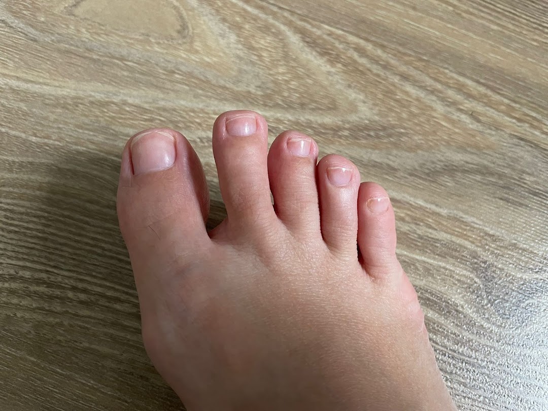 A close-up view of a foot with natural toenails resting on a wooden floor.