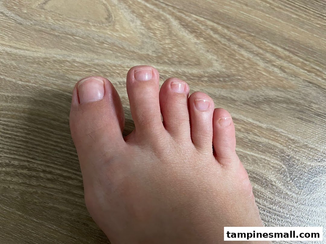 A close-up view of a foot with natural toenails resting on a wooden floor.
