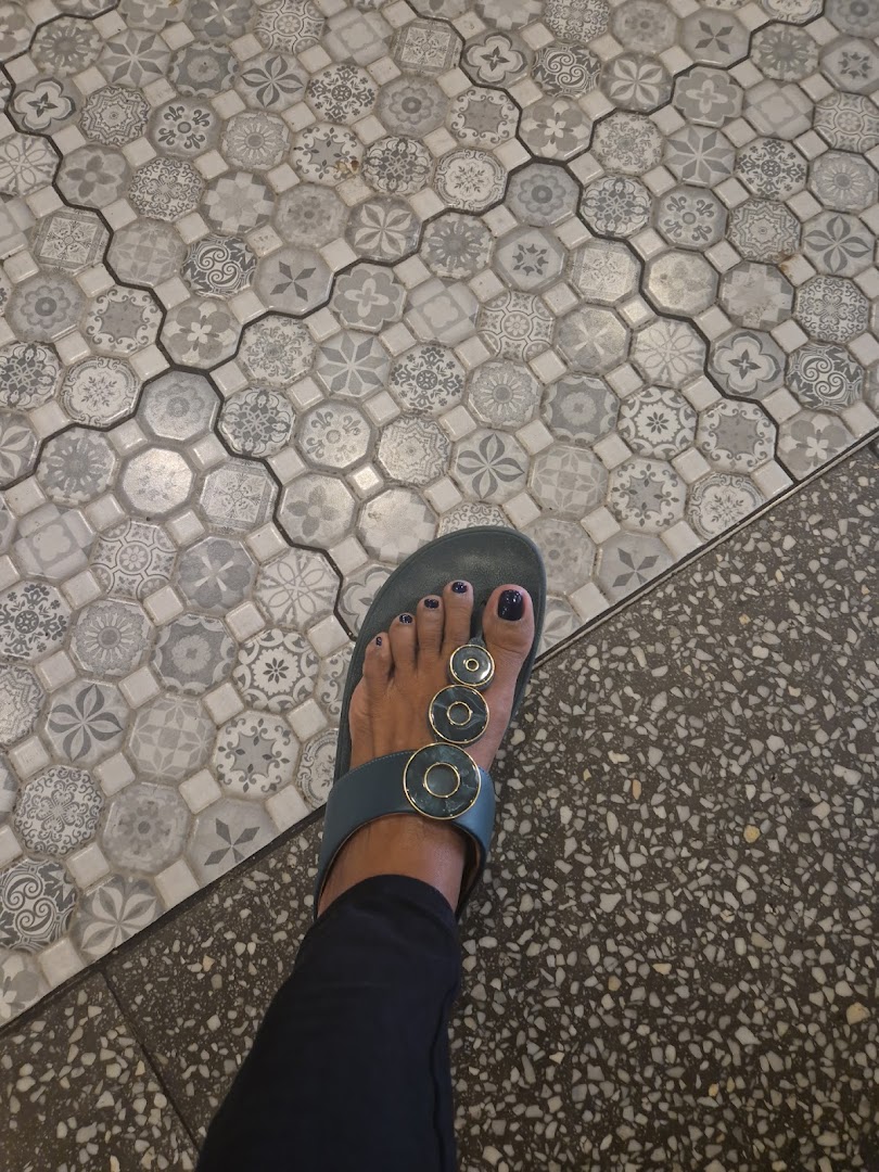 A person's foot in a sandal on a patterned and speckled tiled floor.