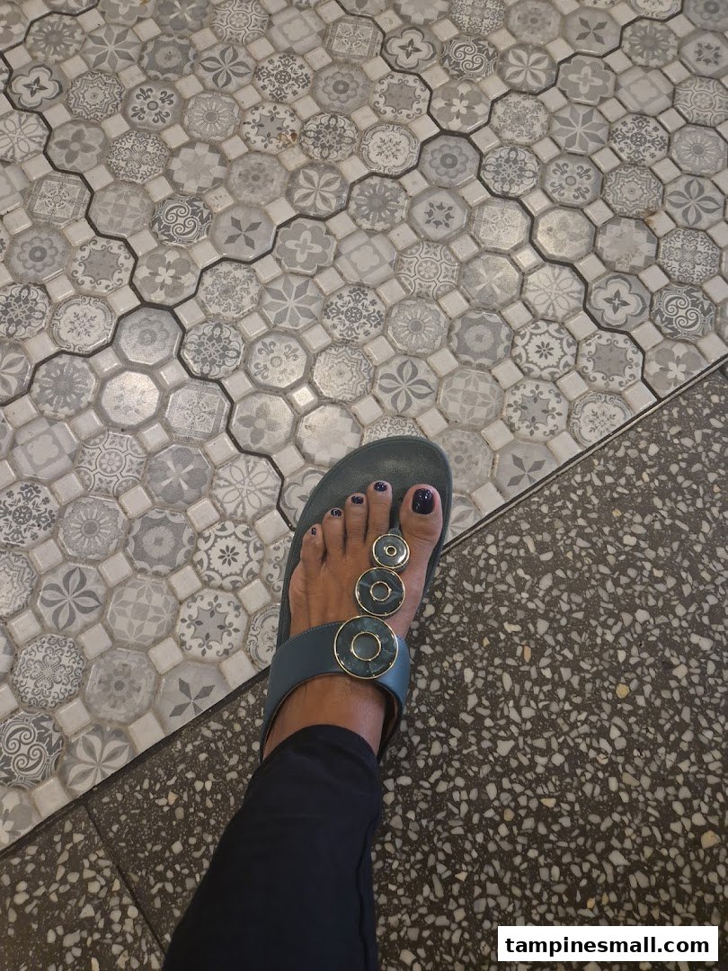 A person's foot in a sandal on a patterned and speckled tiled floor.
