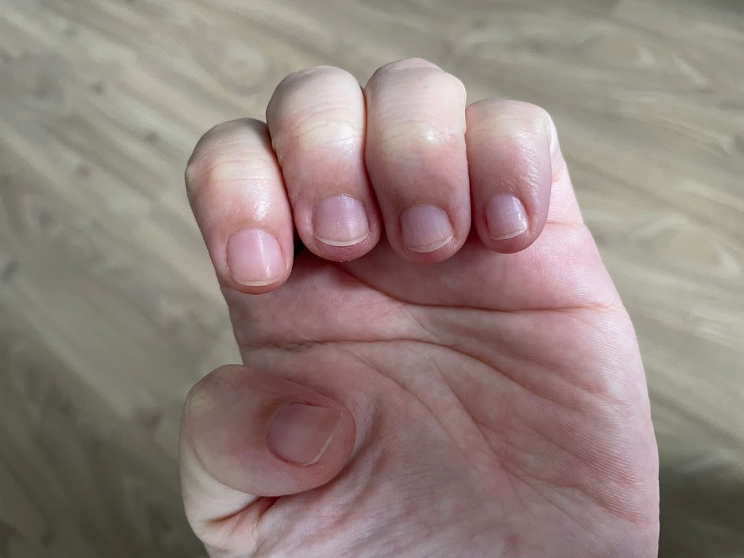 Close-up of a person's hand with visible knuckles and fingernails against a wooden floor.