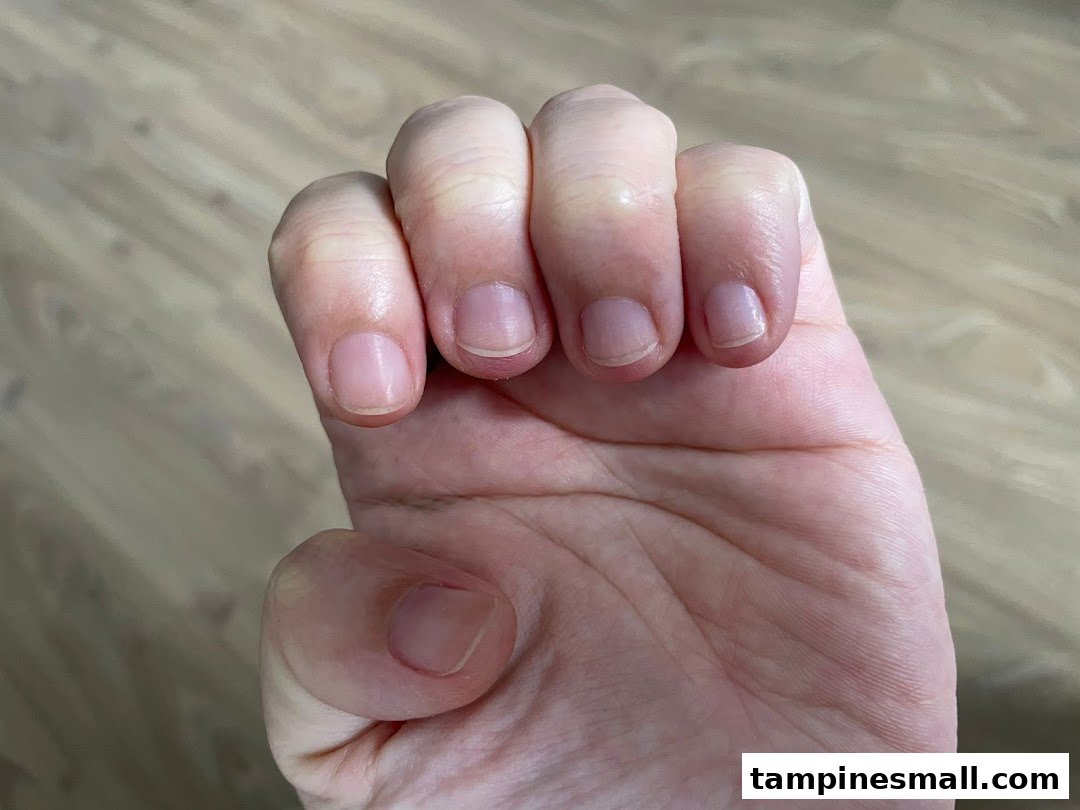 Close-up of a person's hand with visible knuckles and fingernails against a wooden floor.