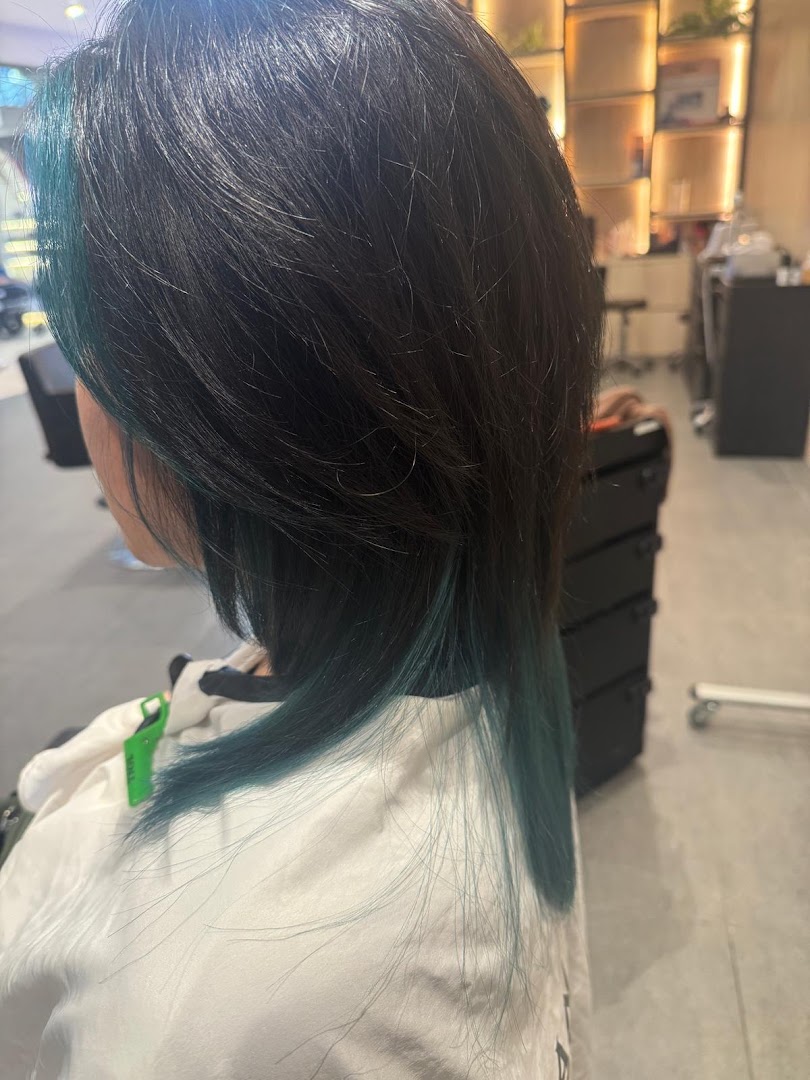 A person with dark hair and vibrant teal highlights, wearing a salon cape, showcasing a hair service.