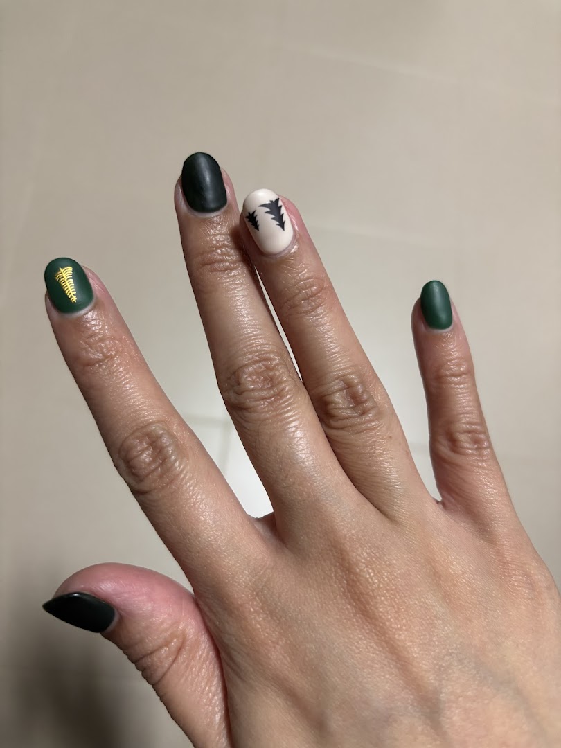 A hand showcasing dark green and cream-colored nails with intricate designs.