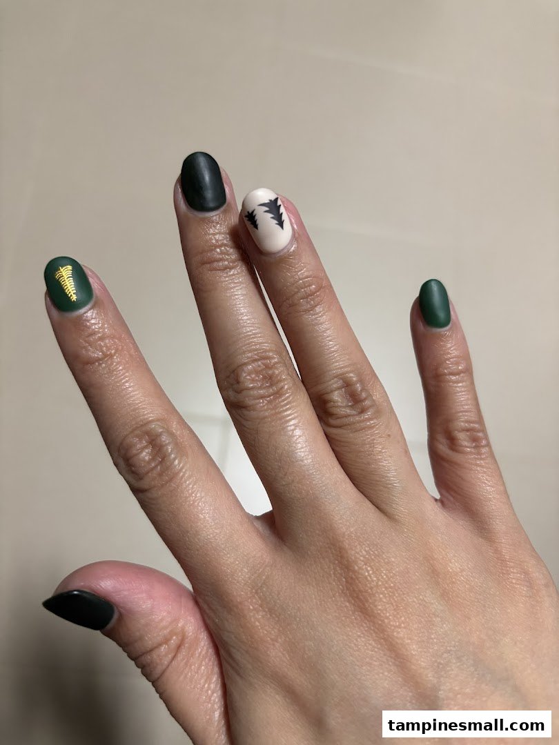 A hand showcasing dark green and cream-colored nails with intricate designs.