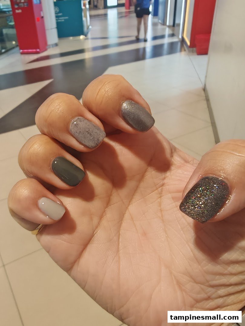 A hand showcasing freshly painted nails with various shades and textures.