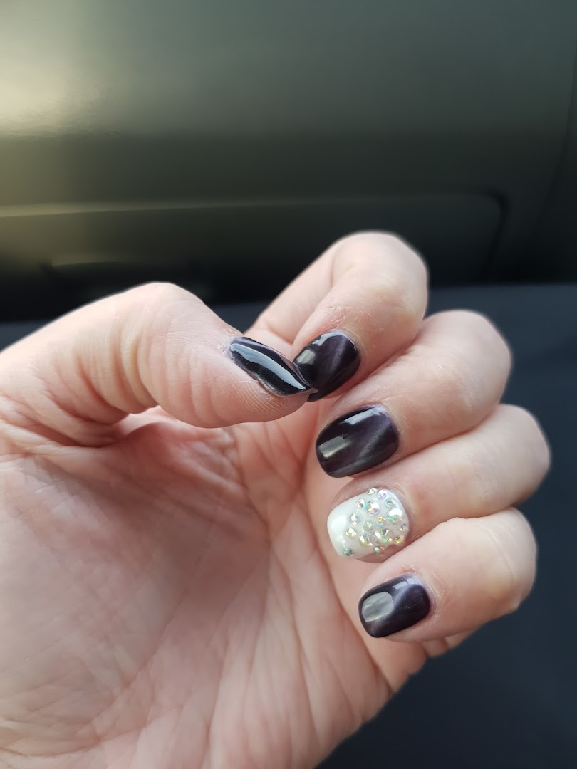 A hand showcasing dark, glossy nails with one accent nail adorned with sparkling rhinestones.