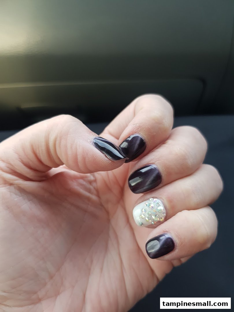 A hand showcasing dark, glossy nails with one accent nail adorned with sparkling rhinestones.
