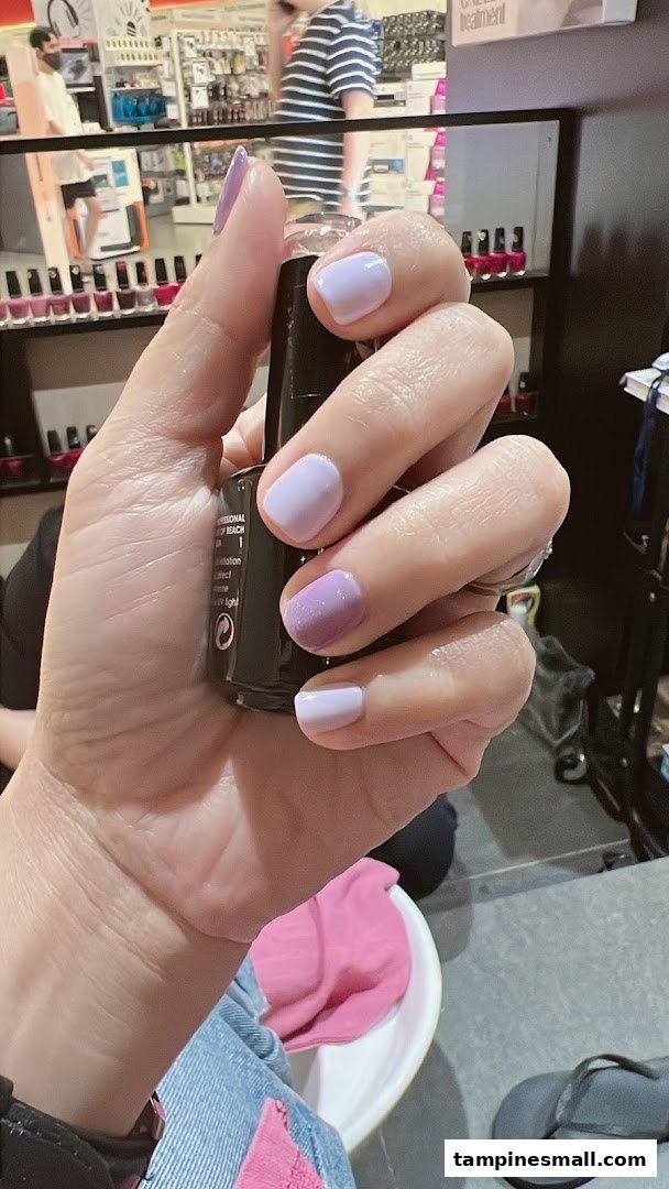 A hand showcasing fresh purple and lavender nail polish, holding a nail polish bottle inside a beauty salon.
