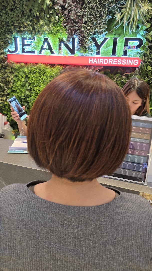 A customer with freshly styled hair at Jean Yip Hairdressing, with staff and salon branding in the background.
