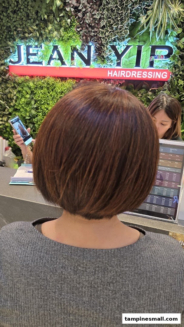A customer with freshly styled hair at Jean Yip Hairdressing, with staff and salon branding in the background.