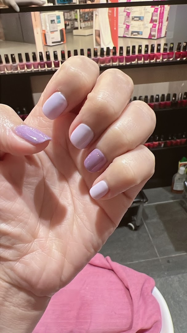 A hand showcasing freshly manicured nails in various shades of purple, with nail polish bottles in the background.