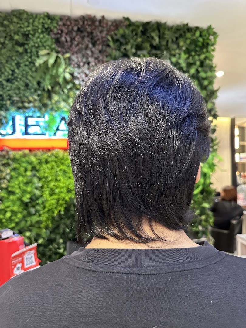 Back view of a person with dark hair inside Jean Yip salon, with a green wall background.