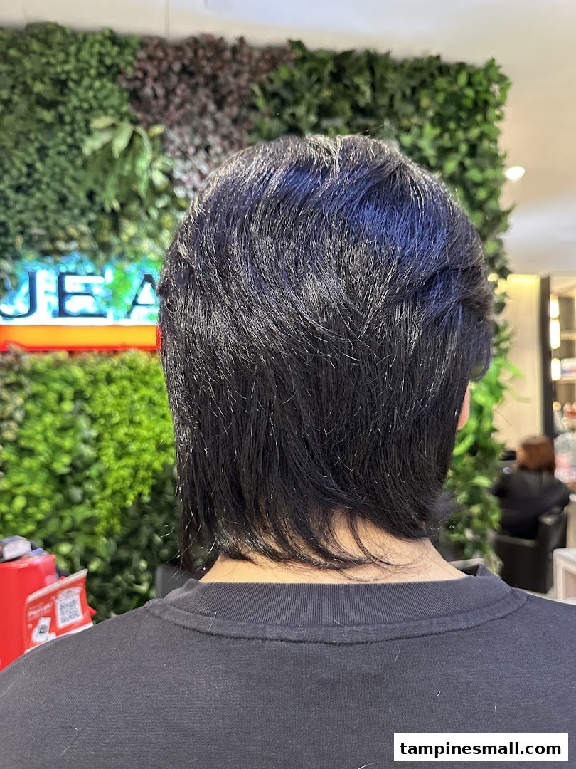 Back view of a person with dark hair inside Jean Yip salon, with a green wall background.