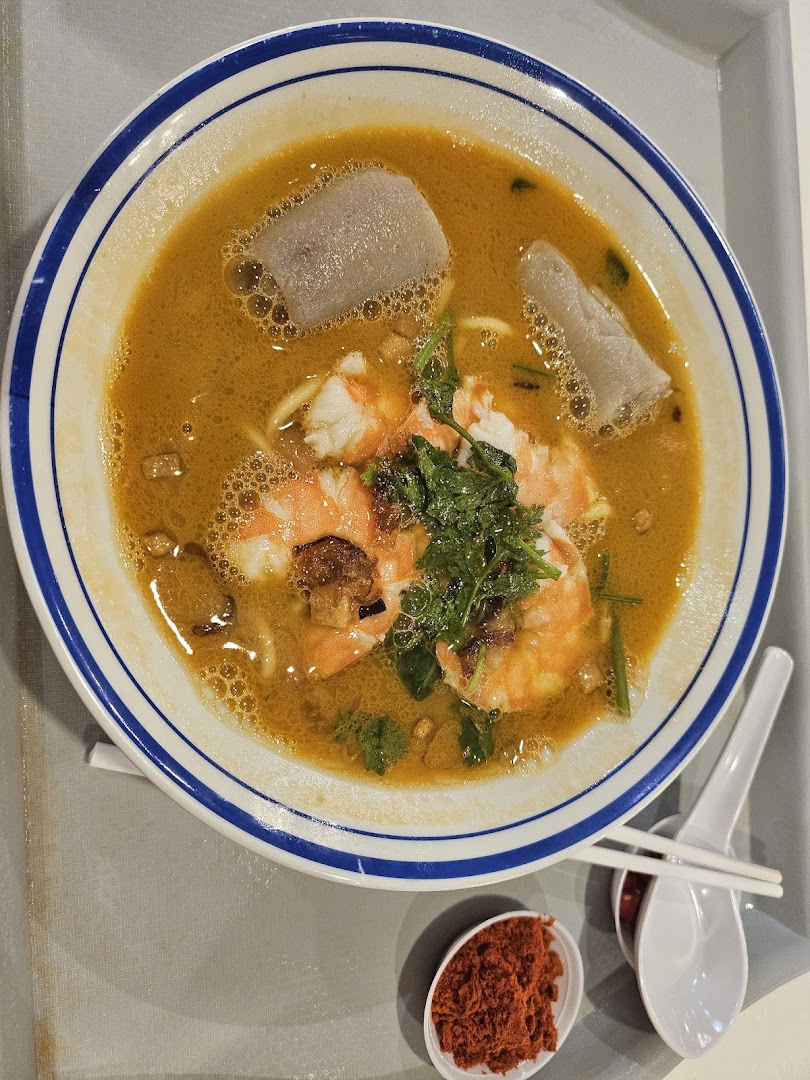 A vibrant bowl of prawn noodles with fresh shrimp and fish cakes, served with chili.