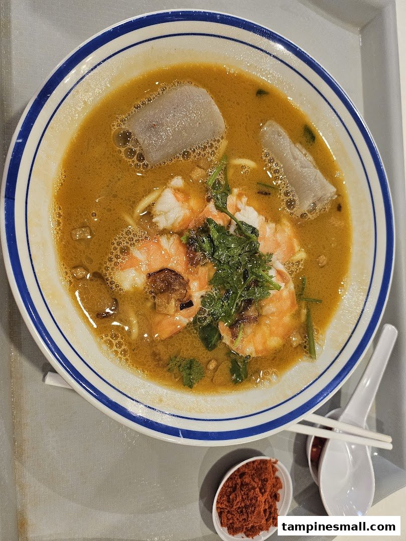 A vibrant bowl of prawn noodles with fresh shrimp and fish cakes, served with chili.