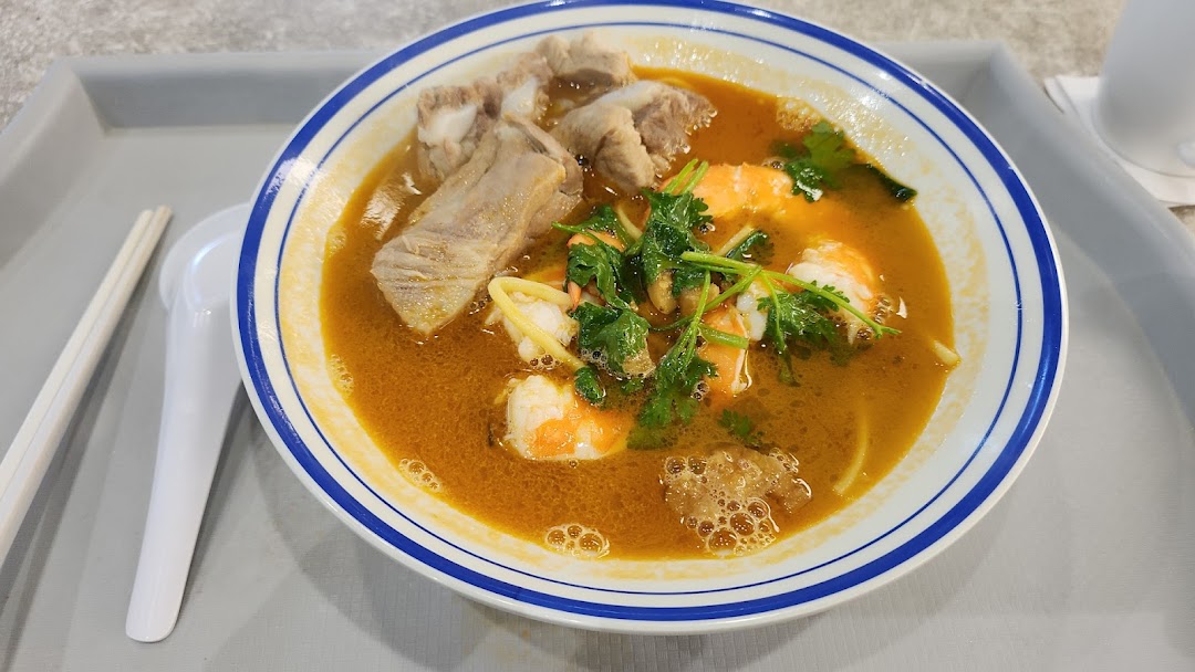 A vibrant bowl of prawn and pork rib noodles with a rich, savory broth and fresh herbs.