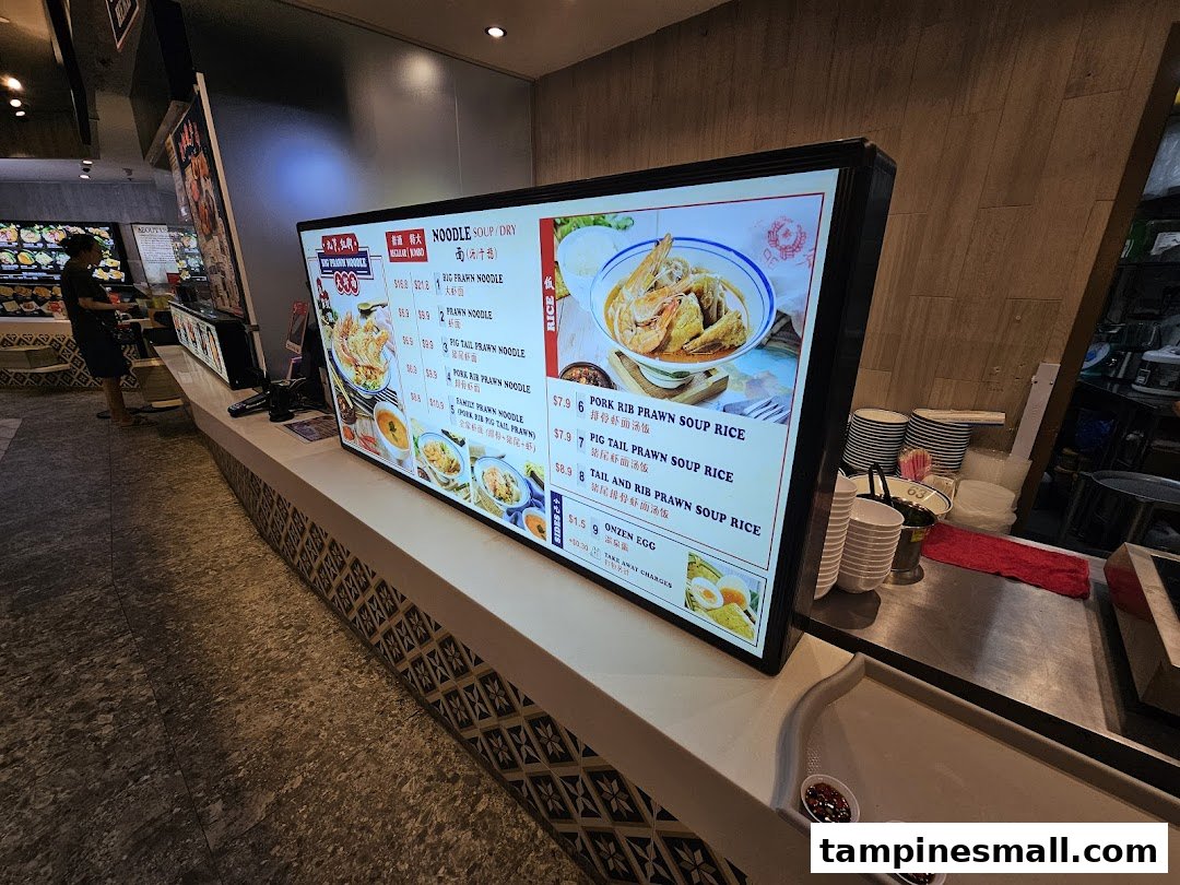 A digital menu board displaying various prawn noodle and rice dishes with prices at Jiaxins Prawn Noodle.