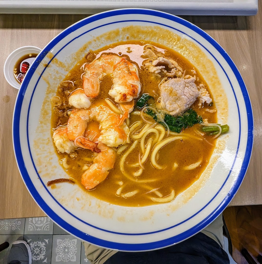 A close-up of a delicious bowl of prawn noodles with shrimp, pork, and greens.