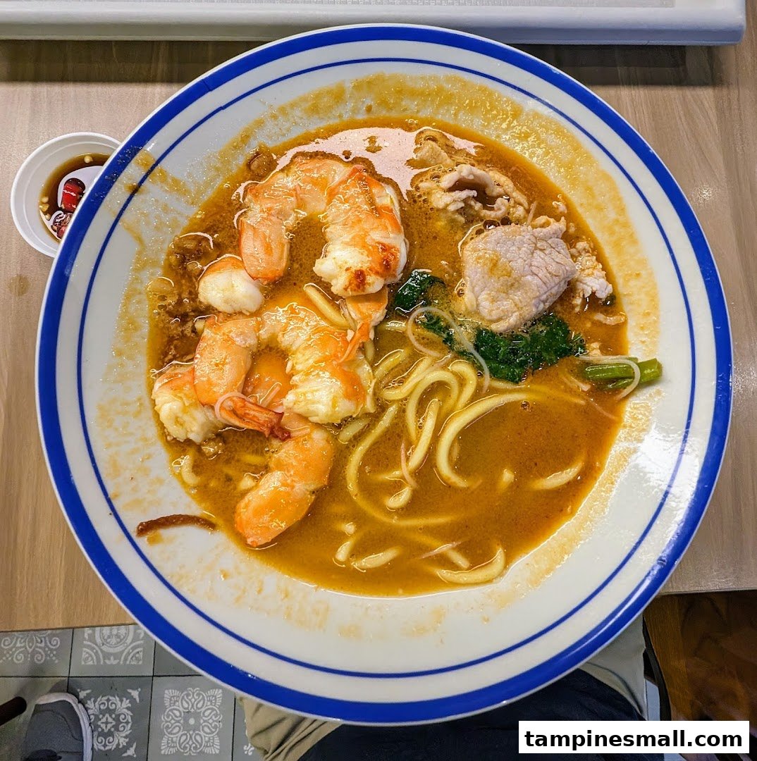 A close-up of a delicious bowl of prawn noodles with shrimp, pork, and greens.