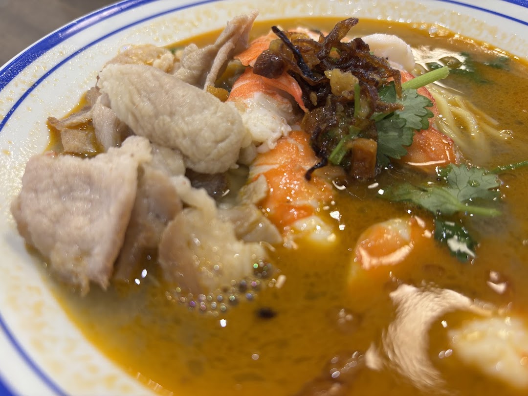 A close-up of a vibrant bowl of prawn noodles with shrimp, meat, and herbs.