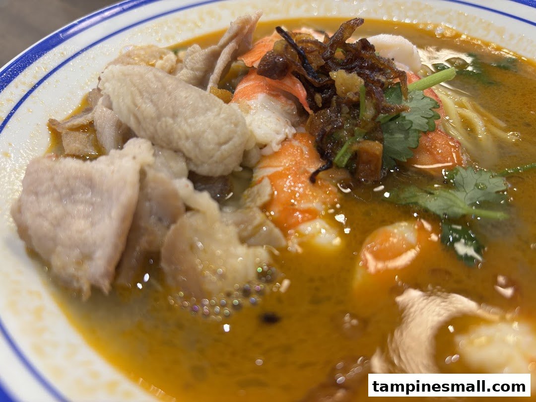 A close-up of a vibrant bowl of prawn noodles with shrimp, meat, and herbs.