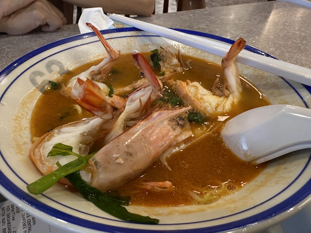 A close-up of a delicious bowl of prawn noodles with large prawns and rich broth.