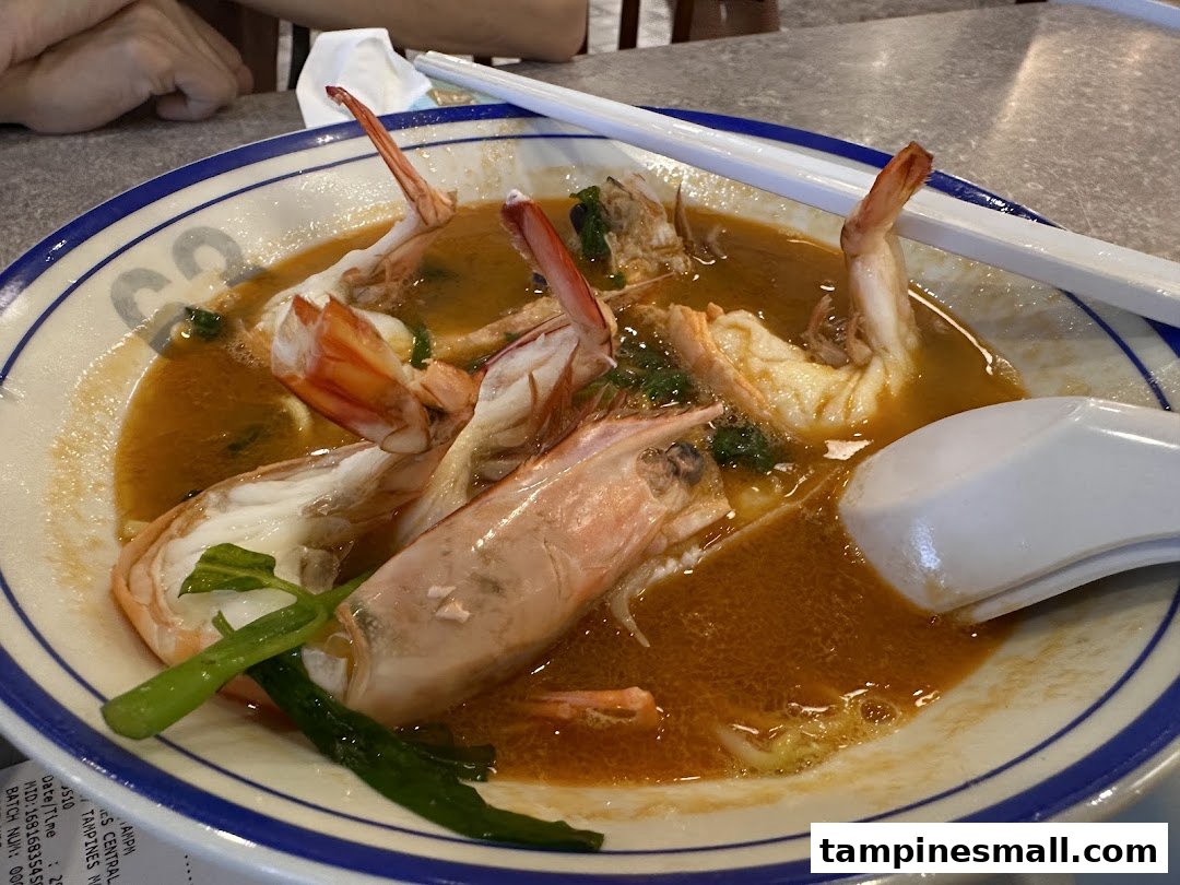 A close-up of a delicious bowl of prawn noodles with large prawns and rich broth.