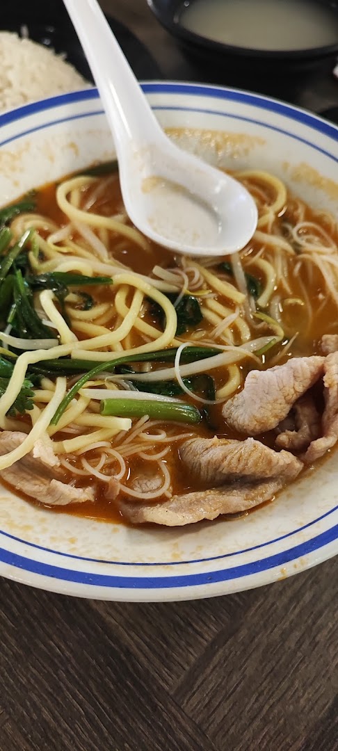 A close-up of a bowl of flavorful noodles with sliced meat, greens, and a spoon.