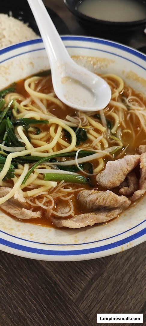 A close-up of a bowl of flavorful noodles with sliced meat, greens, and a spoon.