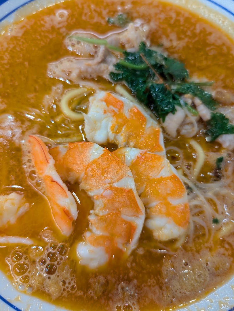 A close-up of a vibrant bowl of prawn noodles with succulent prawns and rich broth.