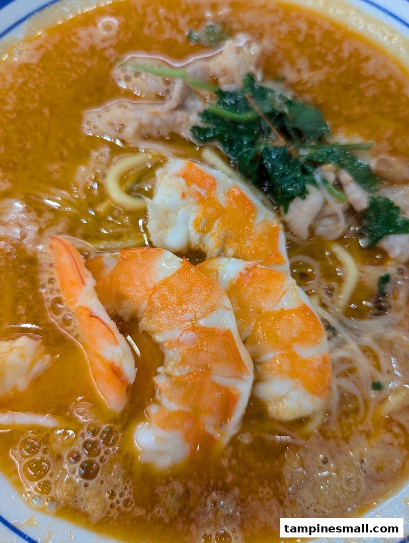 A close-up of a vibrant bowl of prawn noodles with succulent prawns and rich broth.