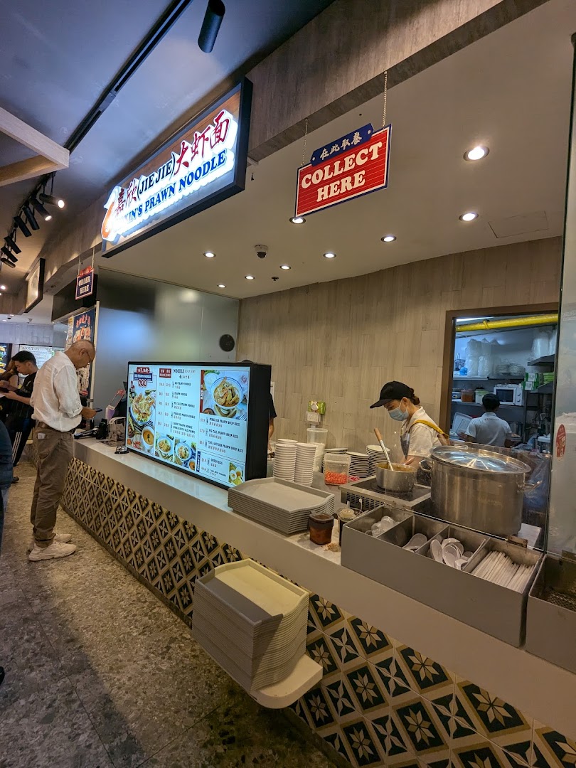 A vibrant counter at Jiaxins Prawn Noodle, with staff preparing food and a customer ordering.
