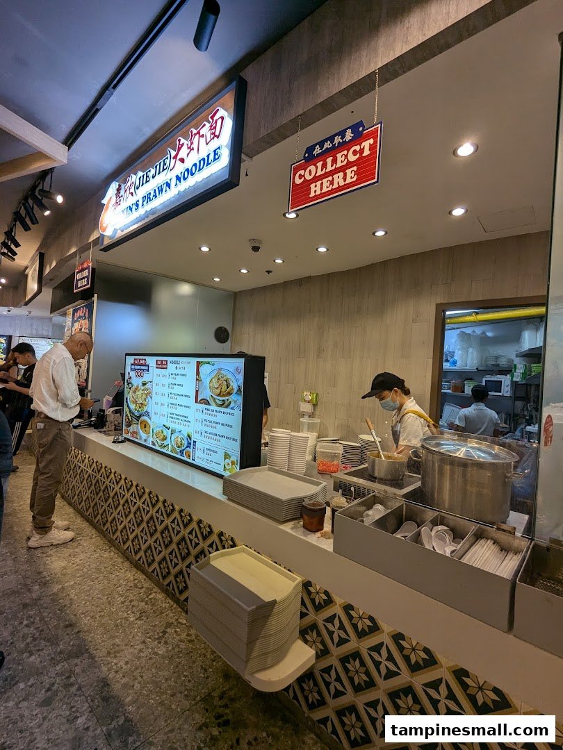 A vibrant counter at Jiaxins Prawn Noodle, with staff preparing food and a customer ordering.