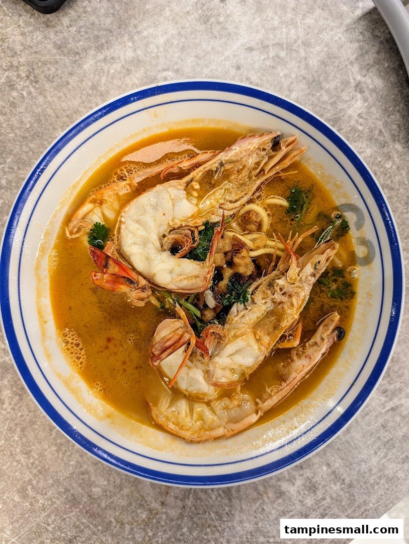 A close-up of a delicious bowl of prawn noodles with large prawns in a rich broth.