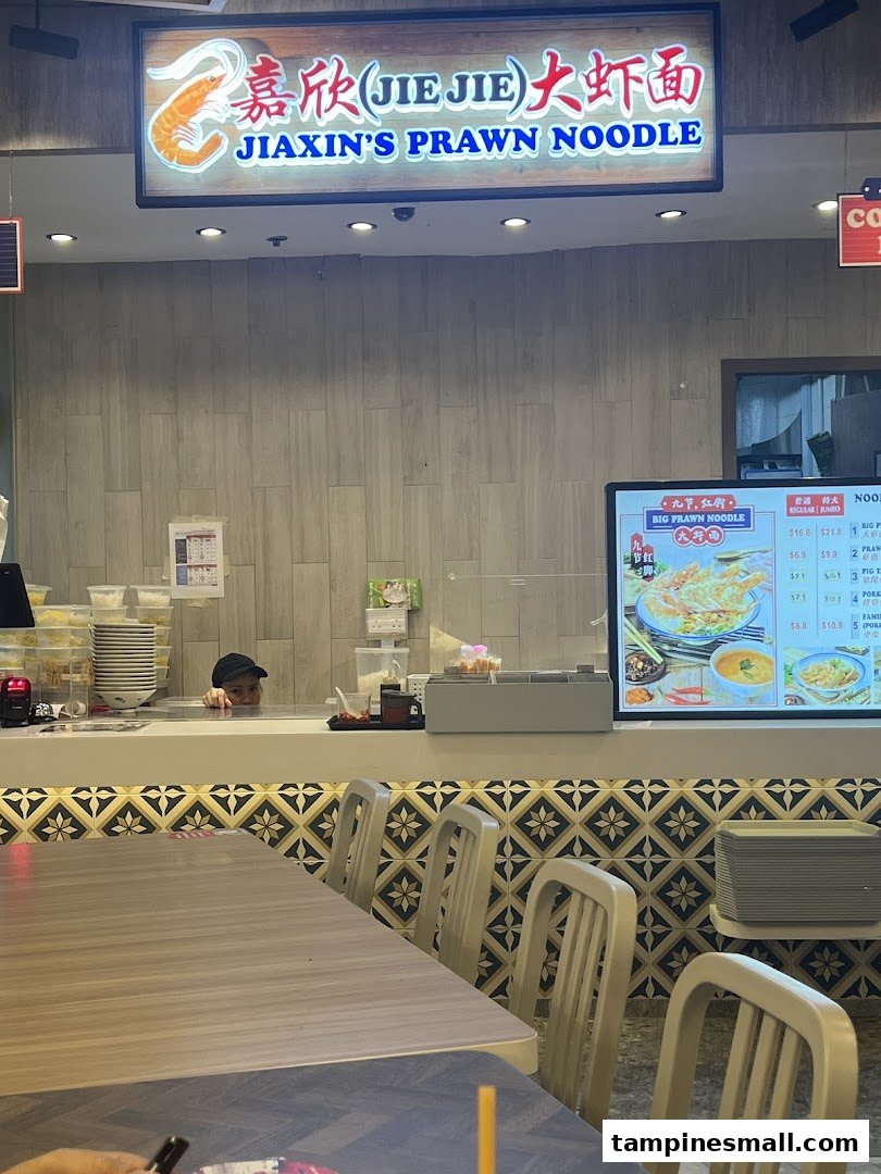 An interior view of Jiaxin's Prawn Noodle shop with a staff member and dining area.