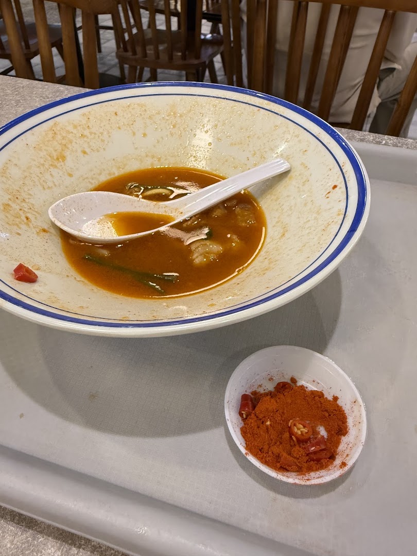 A nearly empty bowl of prawn noodle soup with a side of chili powder on a tray.