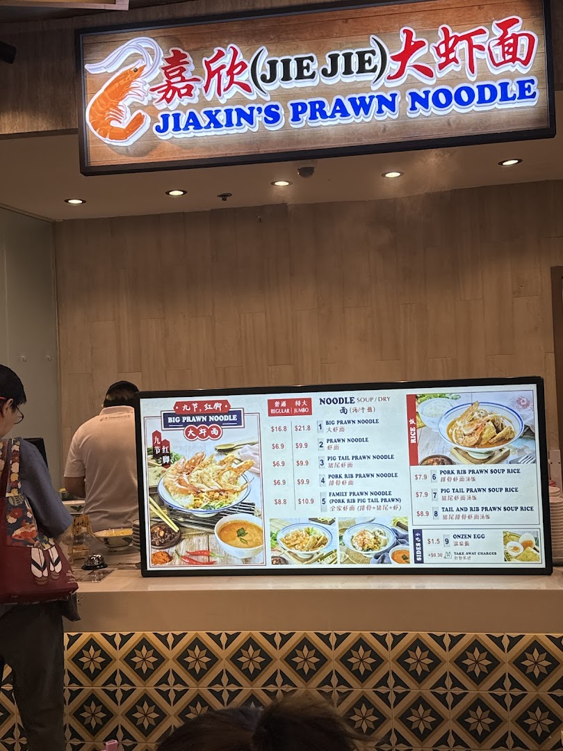 A digital menu board displaying various prawn noodle and rice dishes with prices at Jiaxins Prawn Noodle.