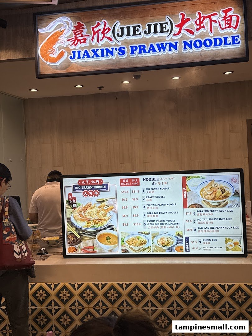 A digital menu board displaying various prawn noodle and rice dishes with prices at Jiaxins Prawn Noodle.
