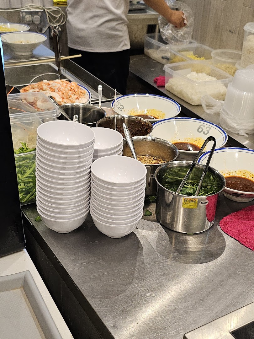 A bustling food stall counter showcasing fresh ingredients and ready-to-serve bowls for delicious prawn noodles.