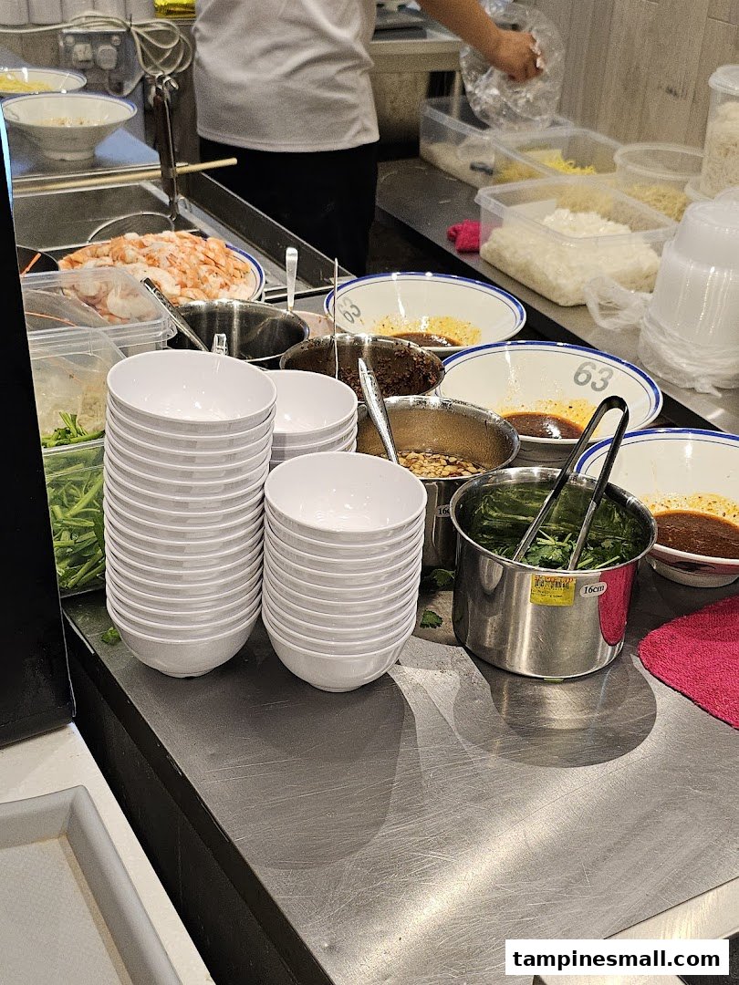 A bustling food stall counter showcasing fresh ingredients and ready-to-serve bowls for delicious prawn noodles.
