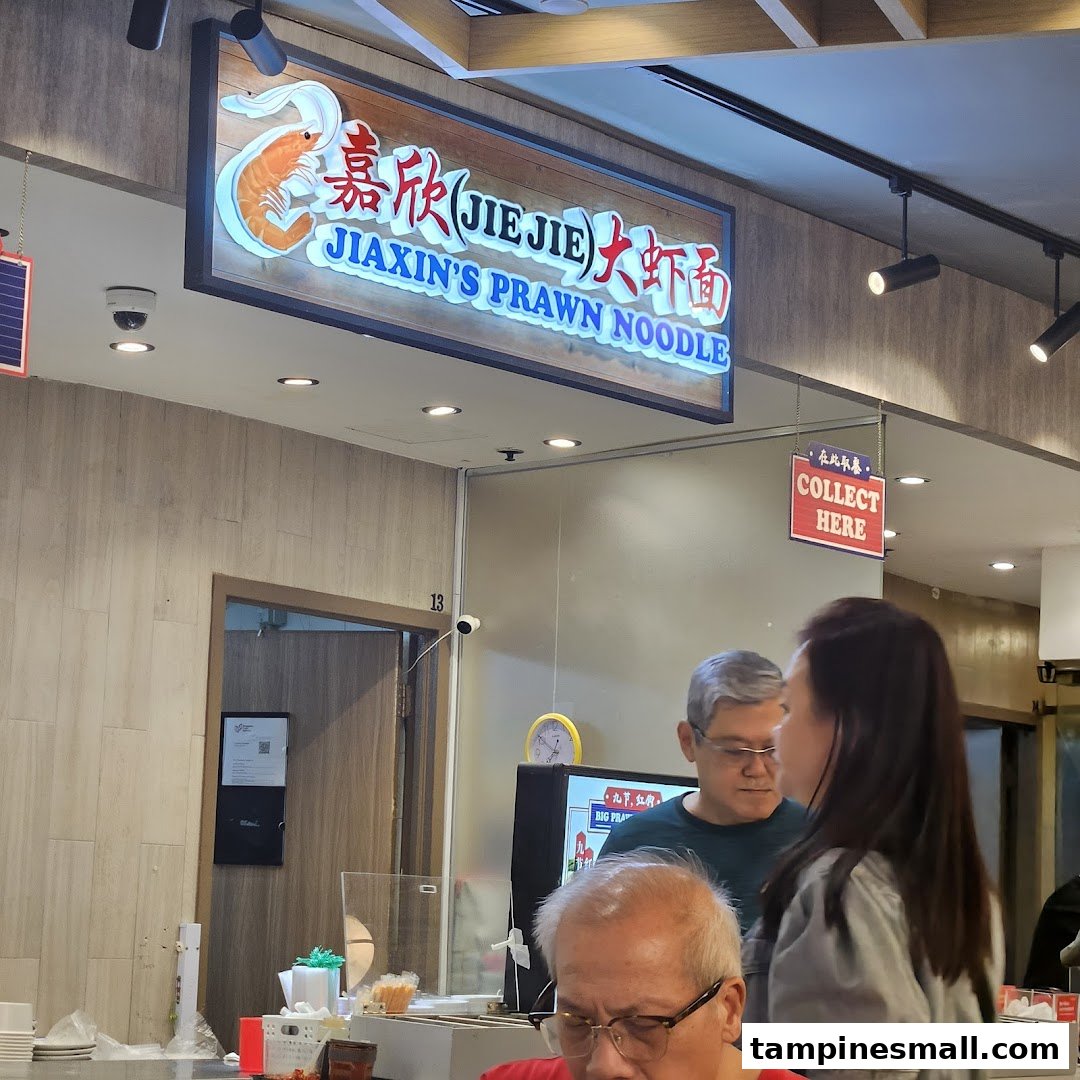 A view of Jiaxin's Prawn Noodle shop sign and service counter with customers.