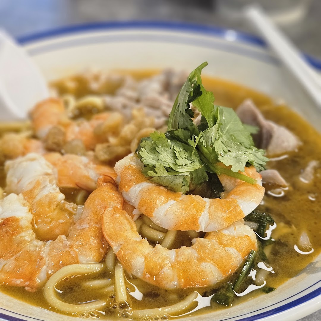 A close-up of a vibrant bowl of prawn noodles with fresh shrimp and cilantro.