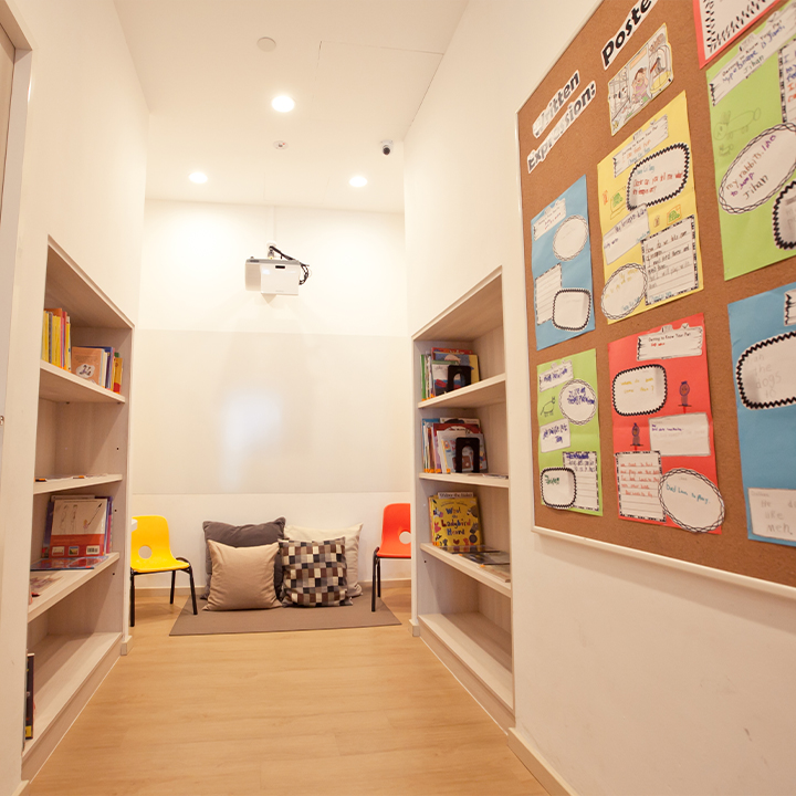 A bright, narrow room with bookshelves, a seating area, a projector, and a bulletin board.