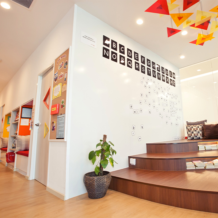 A bright, modern interior of a learning centre featuring an alphabet wall, tiered seating, and a cozy reading nook.