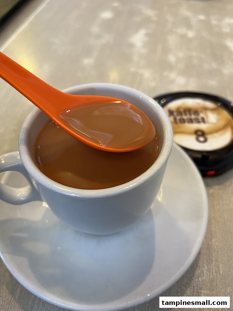 A close-up of a cup of Kaffe Toast's signature beverage with an orange spoon, ready to be enjoyed.