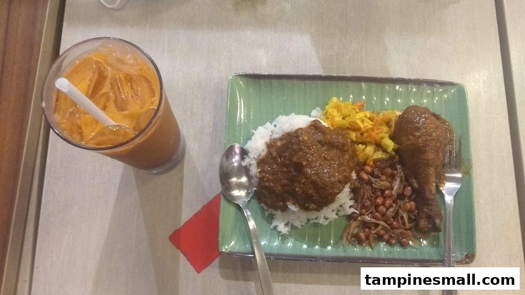 A plate of Nasi Lemak with chicken and a glass of iced milk tea.