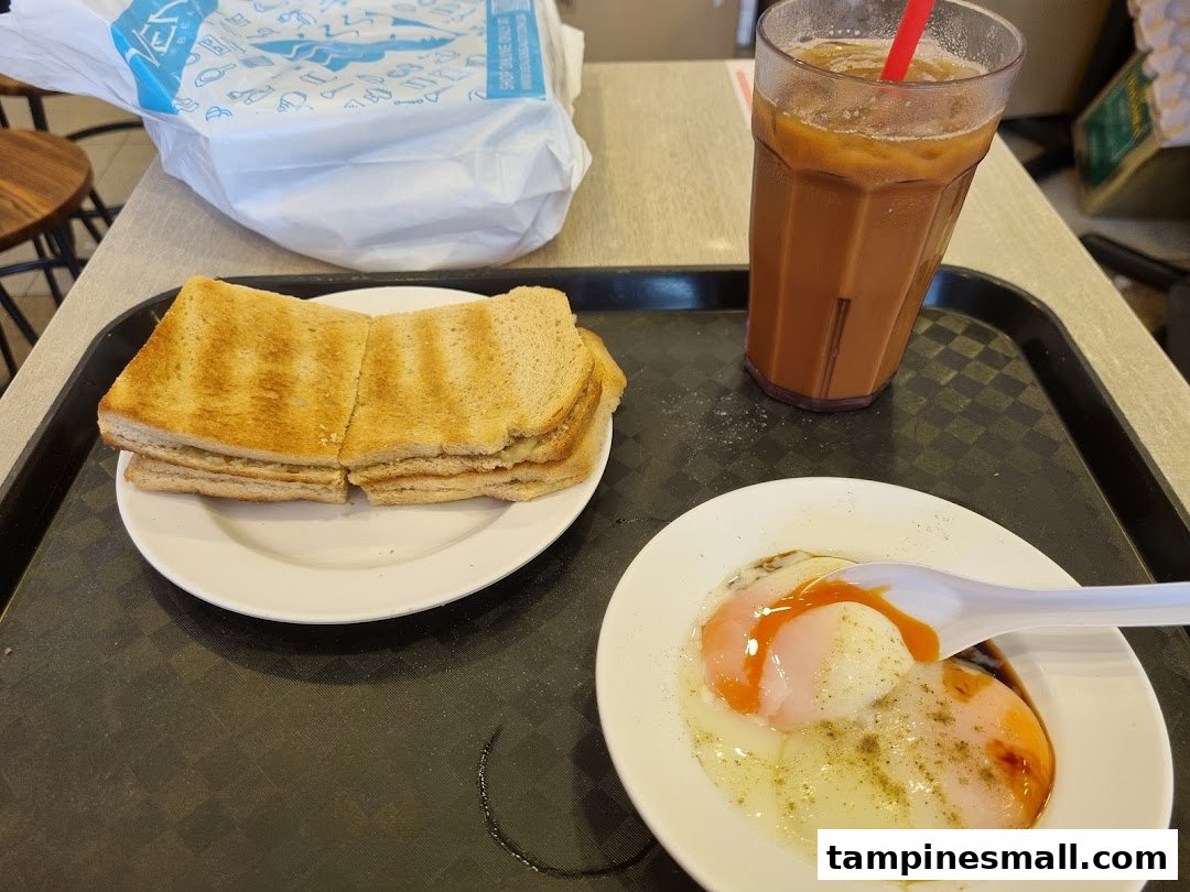 A classic Singaporean breakfast set featuring kaya toast, soft-boiled eggs, and iced coffee.