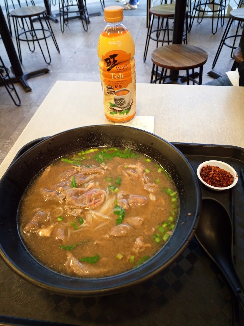 A hearty bowl of beef noodles and a bottle of milk tea on a table at Kaffe Toast.